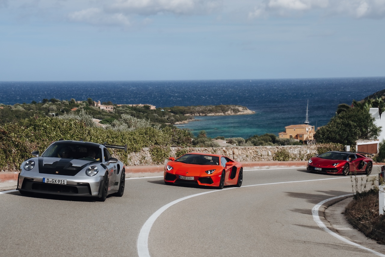 Porsche und Sportwagen auf einer Küstenstraße der Costa Smeralda